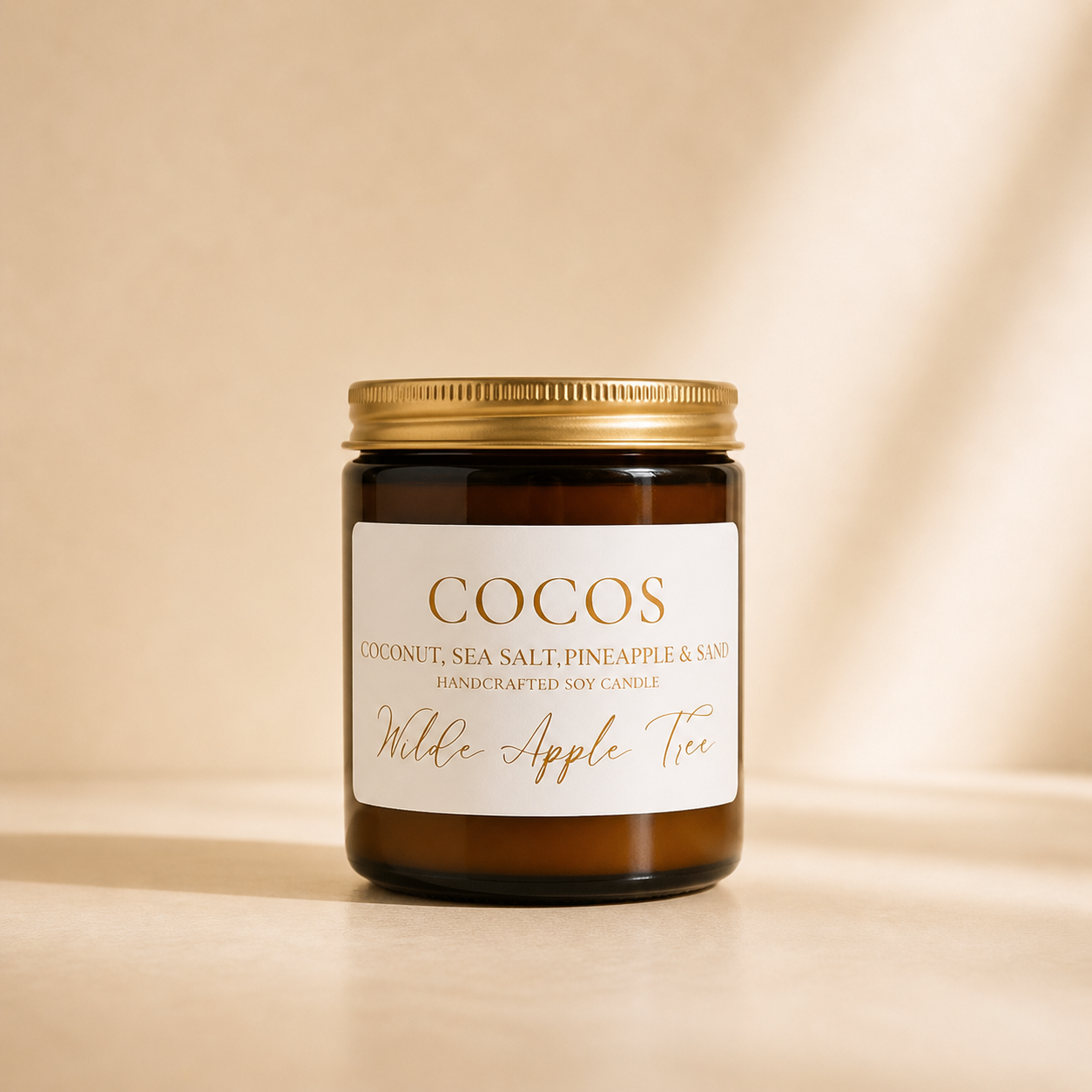 Wilde Apple Tree Cocos medium soy candle in amber glass jar with gold lid against warm fabric backdrop, coconut sea salt and pineapple handcrafted soy candle made in Australia