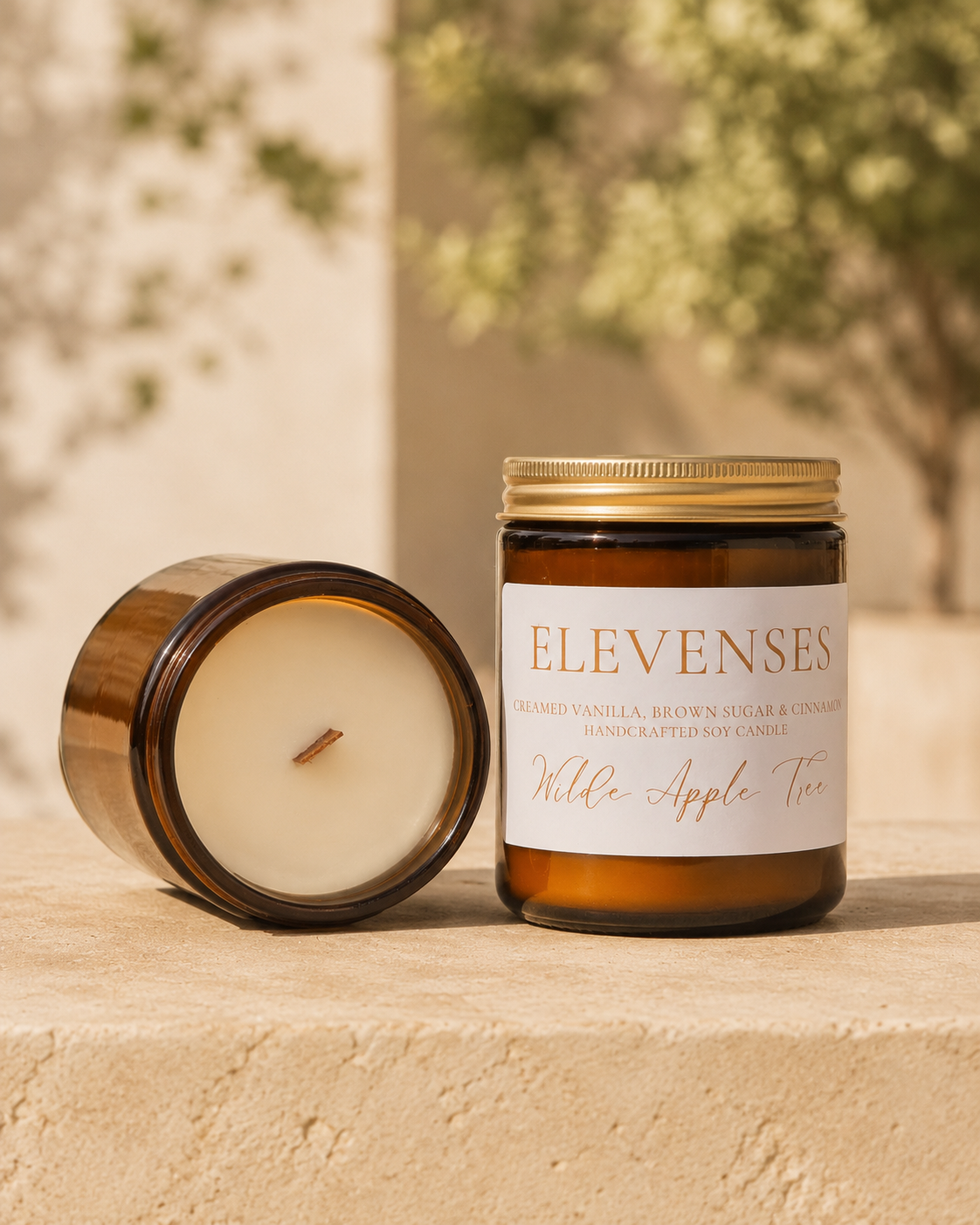 Wilde Apple Tree Elevenses medium soy candle in amber glass jar with lid removed showing natural wooden wick outdoors on stone ledge, creamed vanilla brown sugar and cinnamon scent, handcrafted in Australia