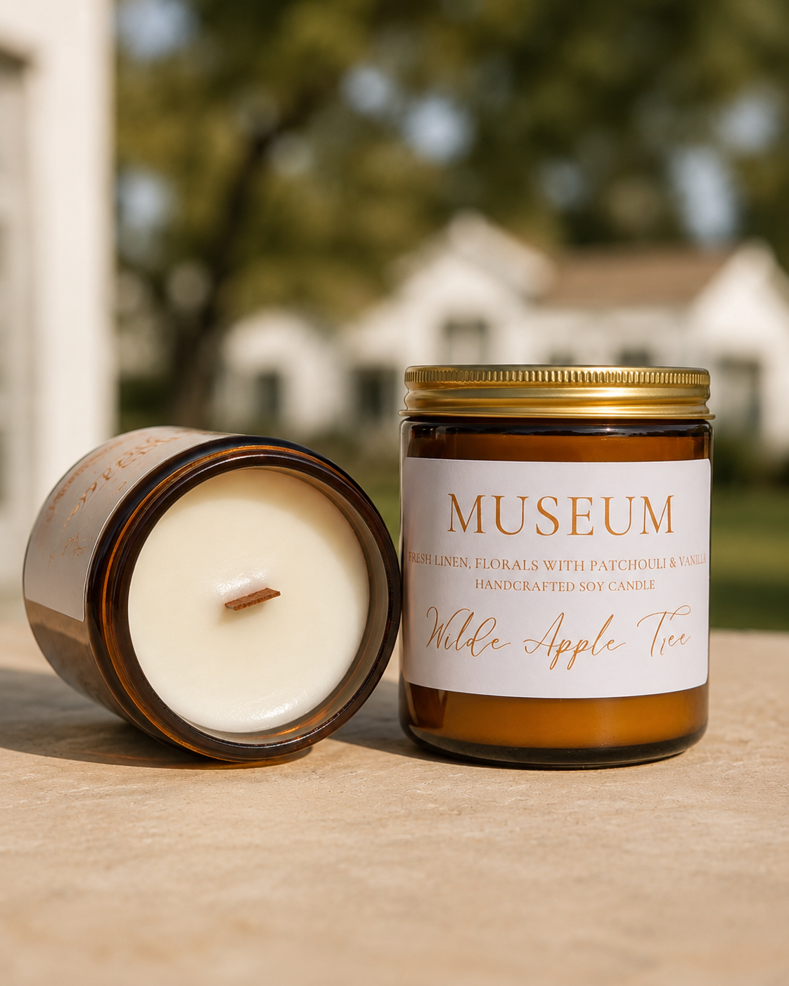Wilde Apple Tree Museum medium soy candle in amber glass jar with lid removed showing natural wooden wick outdoors, fresh linen florals patchouli and vanilla scent, handcrafted in Australia