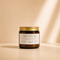 Wilde Apple Tree Museum mini soy candle in amber glass jar with gold lid in warm studio light with soft shadows, fresh linen florals patchouli and vanilla scented handcrafted soy candle made in Australia