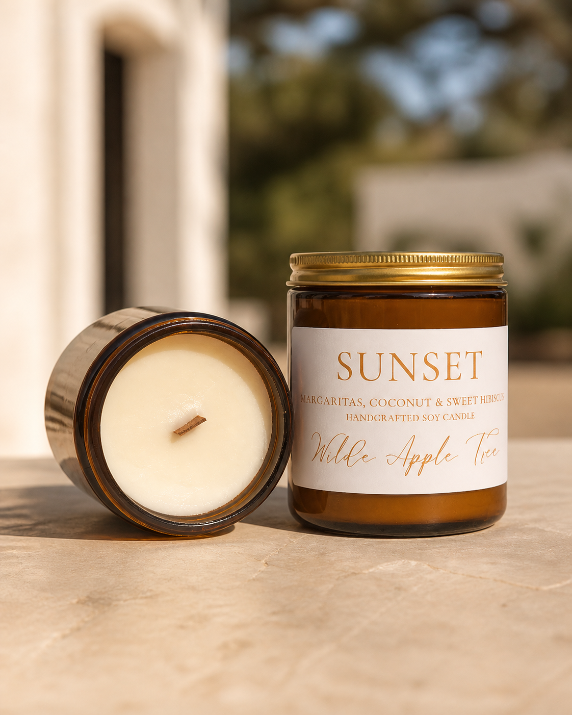 Wilde Apple Tree Sunset medium soy candle in amber glass jar with lid removed showing natural wooden wick outdoors, margarita coconut and sweet hibiscus scent, handcrafted in Australia