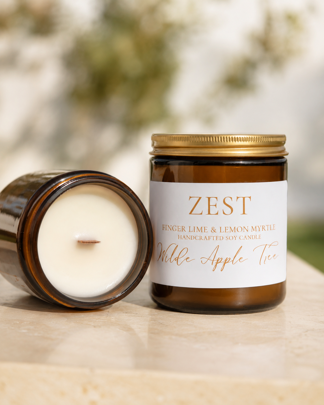 Wilde Apple Tree Zest medium soy candle in amber glass jar with lid removed showing natural wooden wick outdoors, Australian finger lime and lemon myrtle scent, handcrafted in Australia