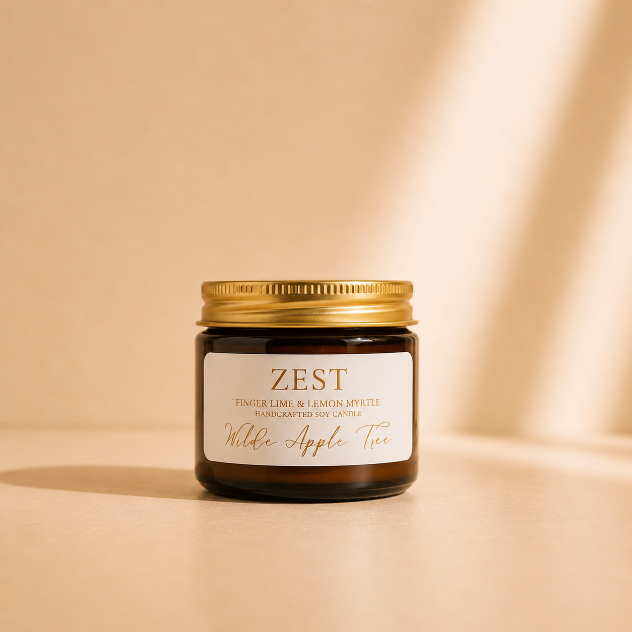 Wilde Apple Tree Zest mini soy candle in amber glass jar with gold lid in warm studio light with soft shadows, Australian finger lime and lemon myrtle scented handcrafted soy candle made in Australia