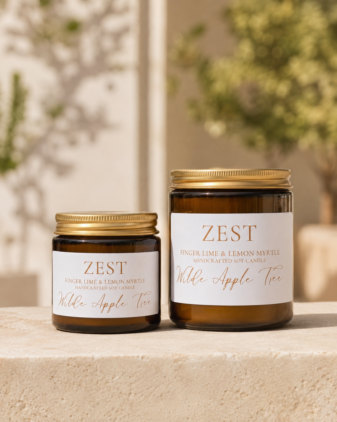 Wilde Apple Tree Zest handcrafted soy candles in mini and medium amber glass jars displayed on stone ledge with garden backdrop, Australian finger lime and lemon myrtle scent, made in Australia